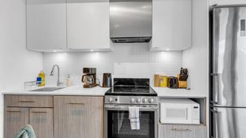 A modern kitchen with white cabinetry, a stainless steel refrigerator, a microwave, and a gas stove.