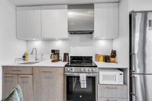 Una cocina moderna con muebles blancos, un refrigerador de acero inoxidable, un microondas y una estufa a gas.