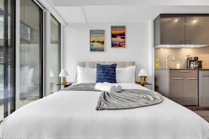Una habitación de hotel moderna con una cama grande, vistas de la ciudad, una kitchenette y dos obras de arte en la pared.