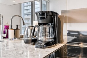 Uma cozinha moderna com uma cafeteira preta, um jarro de vidro e uma geladeira de aço inoxidável.