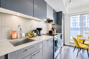 Een moderne keuken met grijze kastjes, een roestvrijstalen spoelbak en een eethoek met gele stoelen.