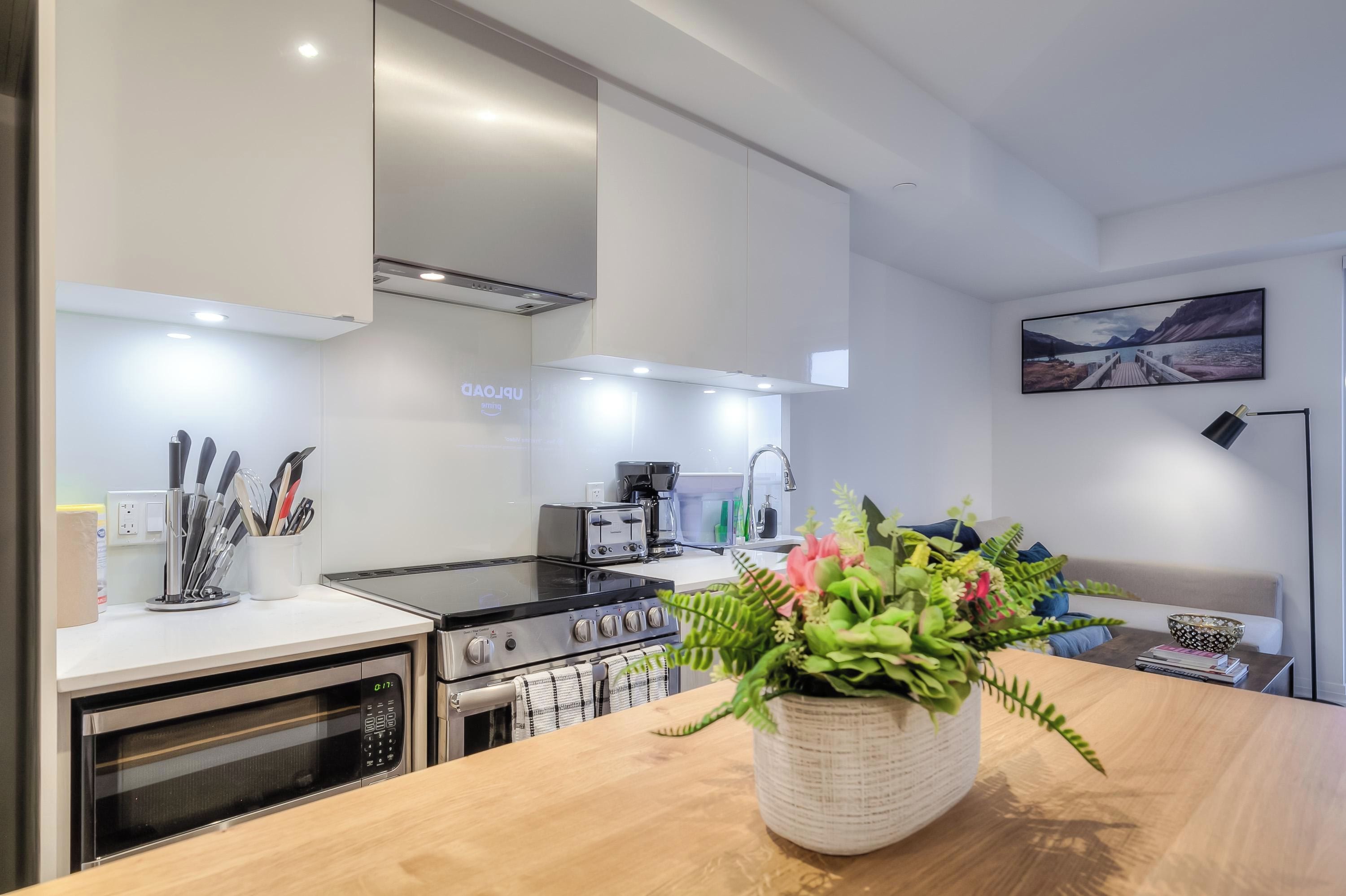 Une cuisine moderne équipée d’un four encastré, d’une cuisinière et d’une machine à café. Un vase rempli de fleurs est posé sur le plan de travail.