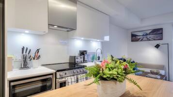 Une cuisine moderne équipée d’un four encastré, d’une cuisinière et d’une machine à café. Un vase rempli de fleurs est posé sur le plan de travail.