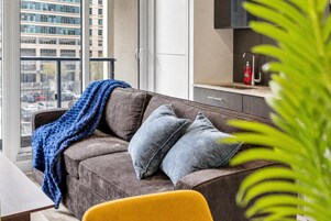 Een moderne woonkamer met een bank, een blauwe plaid en een gele fauteuil.