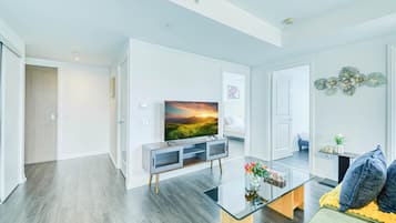 A modern living room with a flat-screen TV, a glass coffee table, and a sofa with cushions.