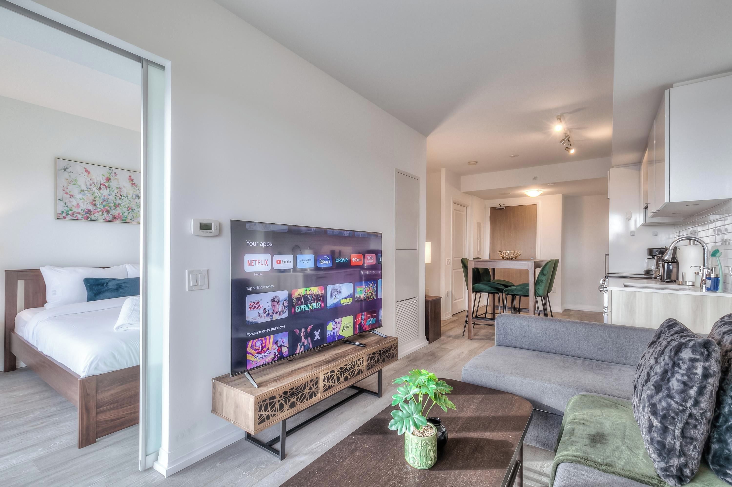 A modern living room with a flat-screen TV, a sofa, a coffee table, and a dining area in the background.
