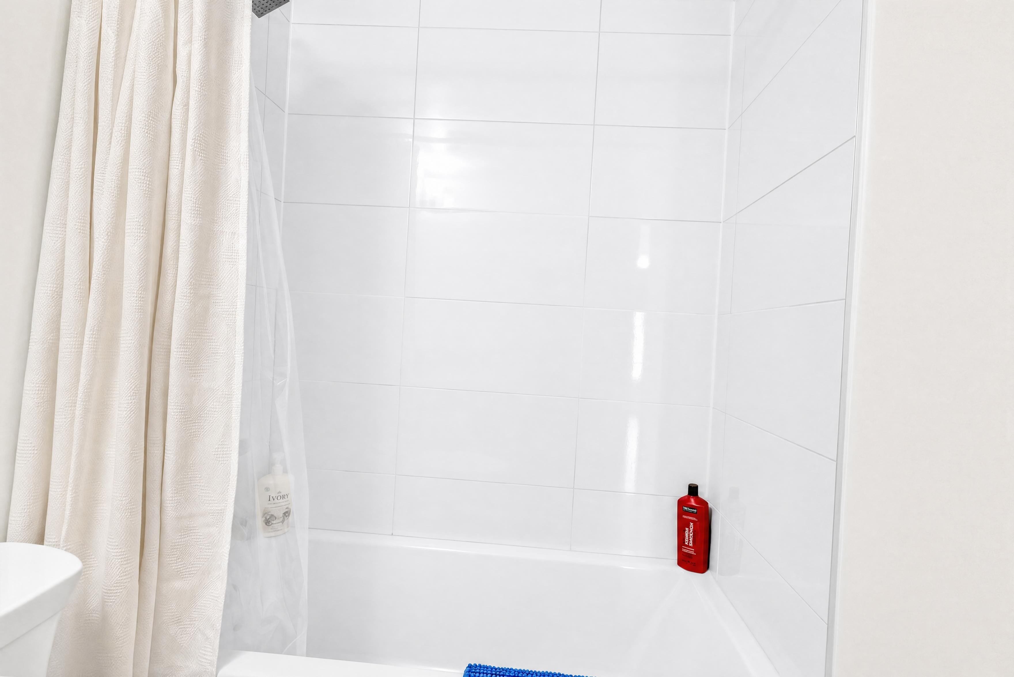 A bathroom with white tiled walls, a white bathtub, and a shower curtain.