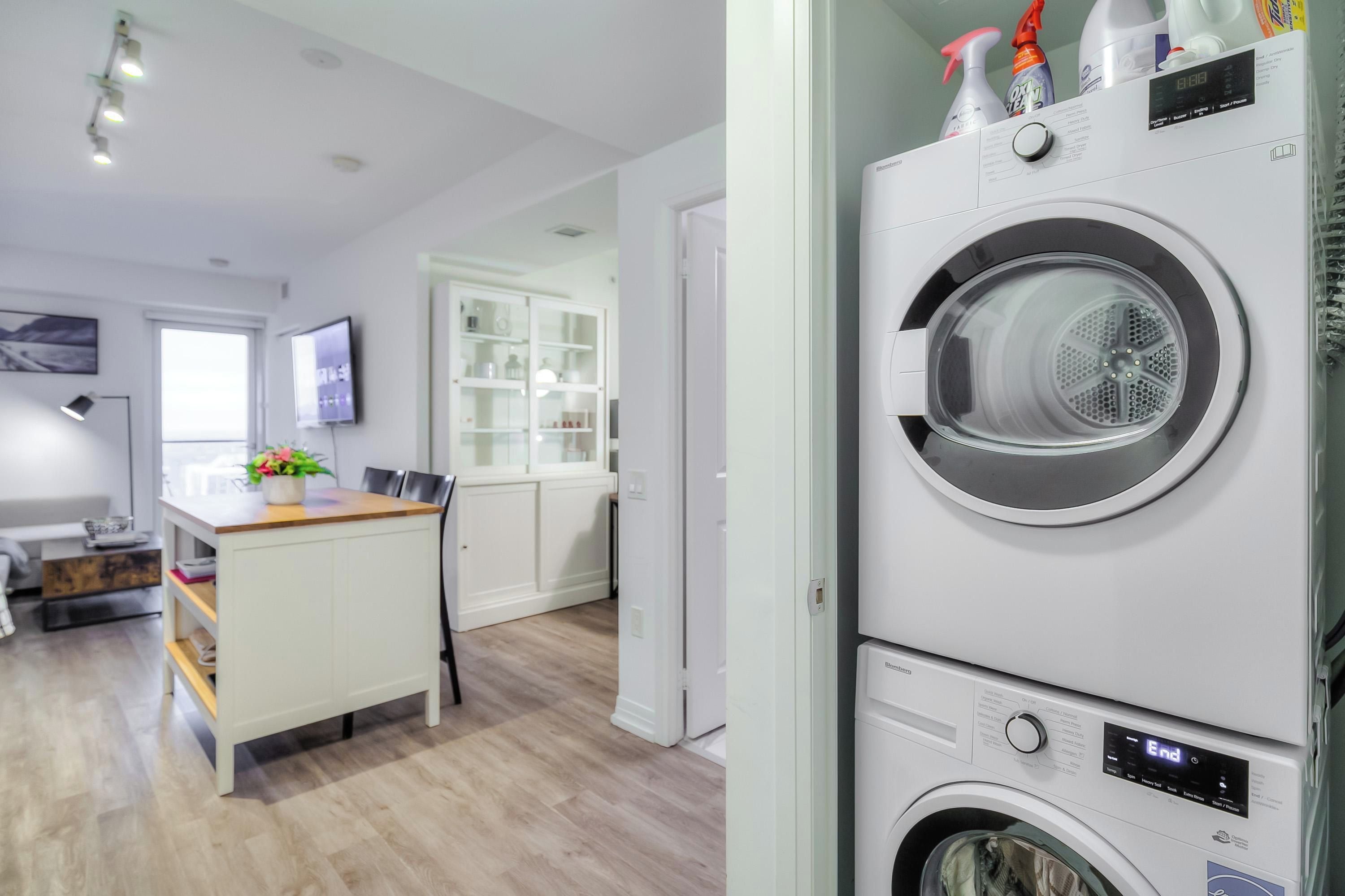 A modern laundry room with stacked washers and dryers, a wooden bench, and a television.