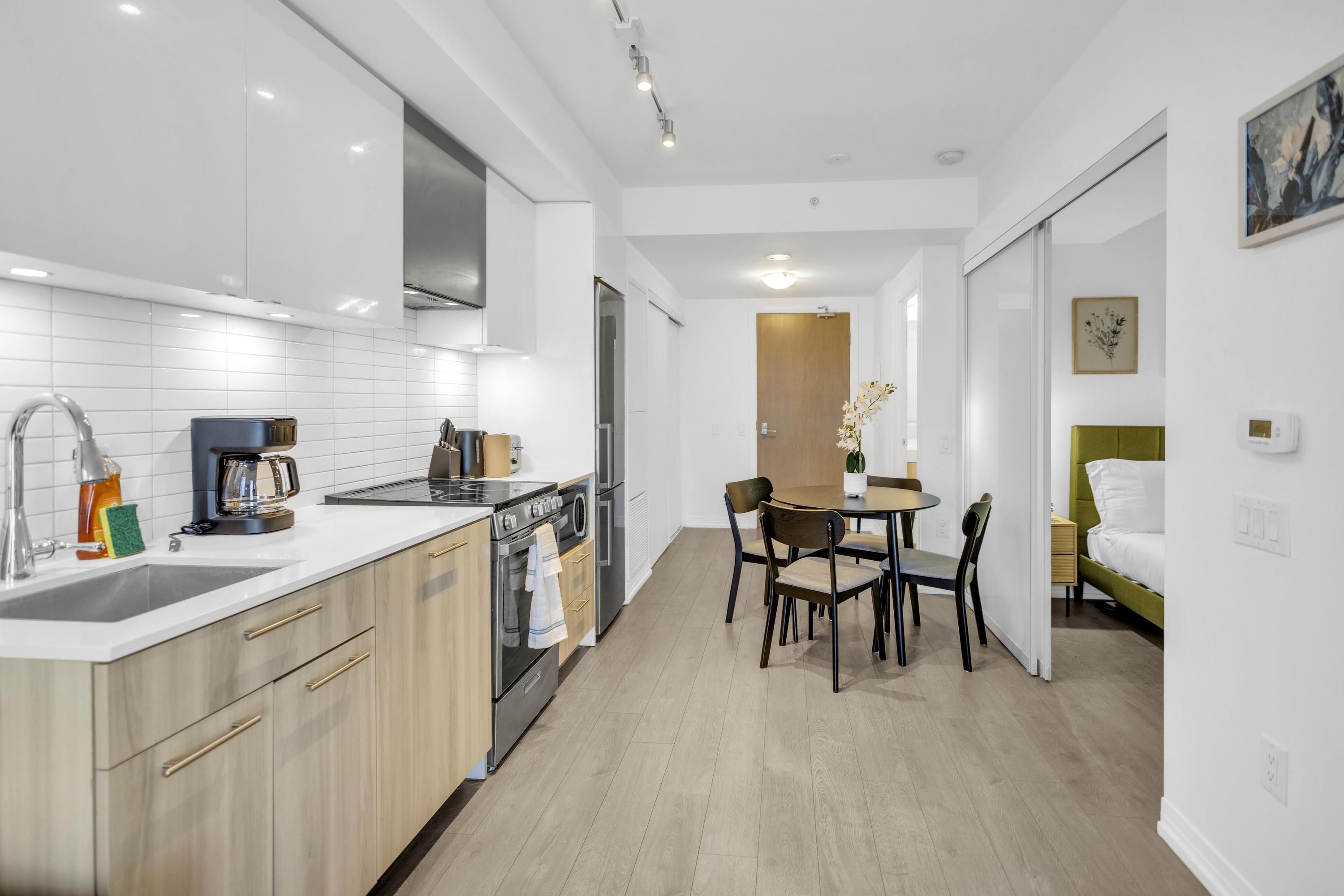 A modern kitchen with a dining area, a small table, and a bed with a green headboard.