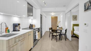 A modern kitchen with a dining area, a small table, and a bed with a green headboard.