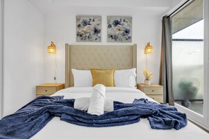 Een hotelkamer met een groot bed, twee nachtkastjes, een raam met gordijnen en twee wandlampen.