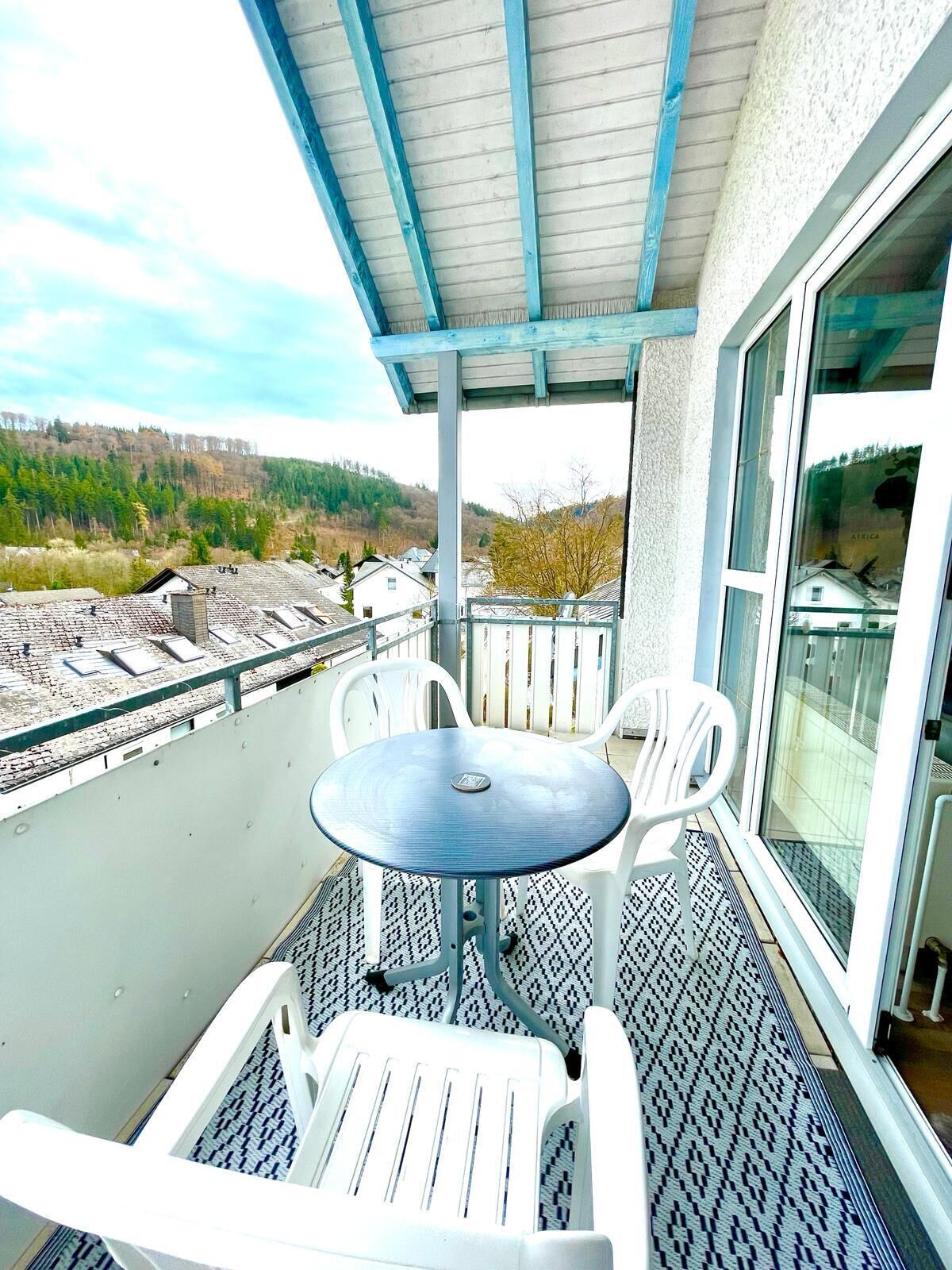Varanda com mesa e cadeiras, com vista para uma área arborizada.