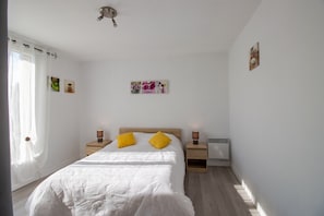 Une chambre à coucher comprenant un lit, deux tables de chevet, une commode, une fenêtre avec des rideaux et des œuvres d’art murales.