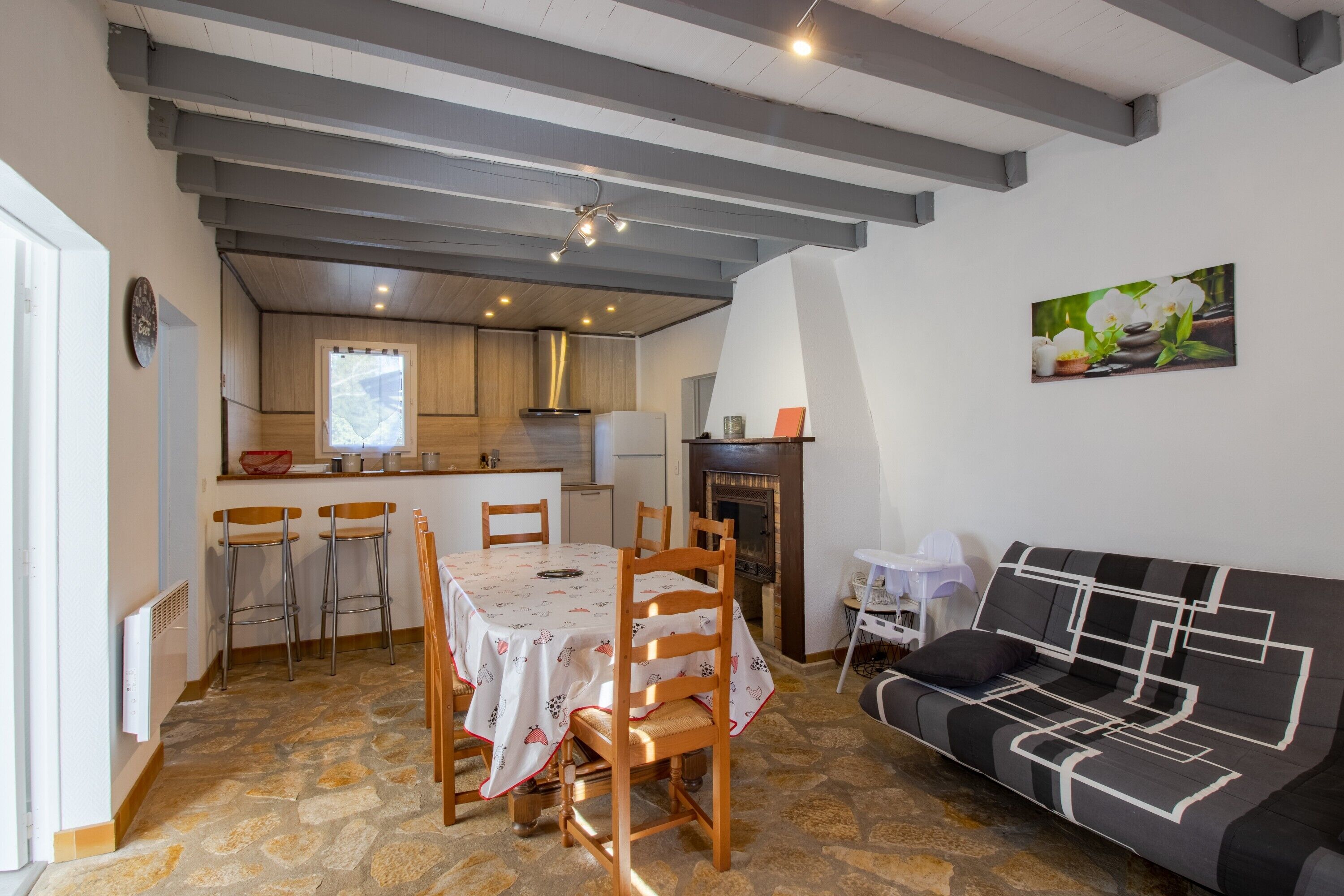 A dining area with a table and chairs, a sofa, a fireplace, and a kitchen in the background.