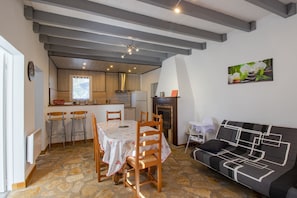 Un espace repas avec une table et des chaises, un canapé, une cheminée et, au fond, une cuisine.