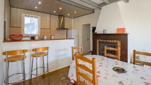A kitchen with wooden cabinets, a window, and a fireplace. There are two bar stools and a table with a patterned tablecloth. - Gîte La Salamandre – Renovated Haven of Peace near Sarlat (Saint-André-d'Allas)