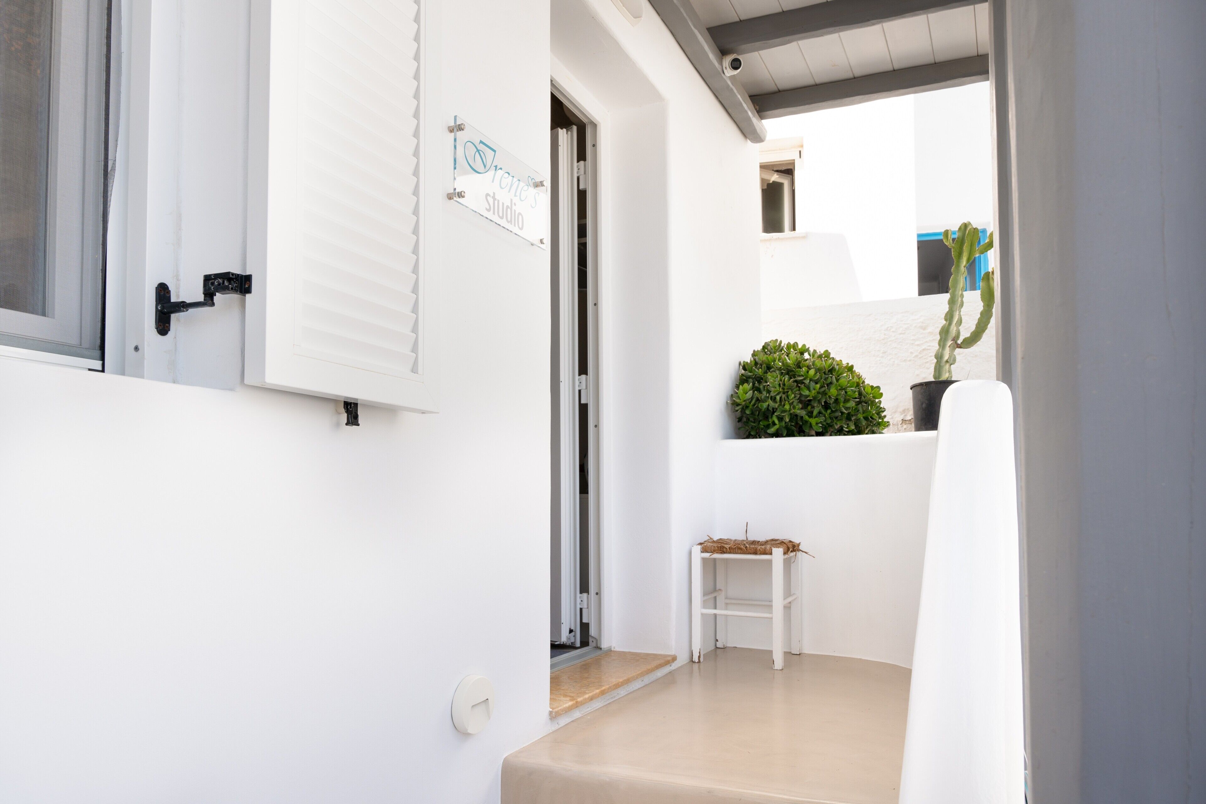 A white exterior wall with a door, a small white shelf with a plant, and a potted cactus.