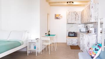 A compact room with a bed, a small dining table with chairs, a kitchenette, and a sofa.