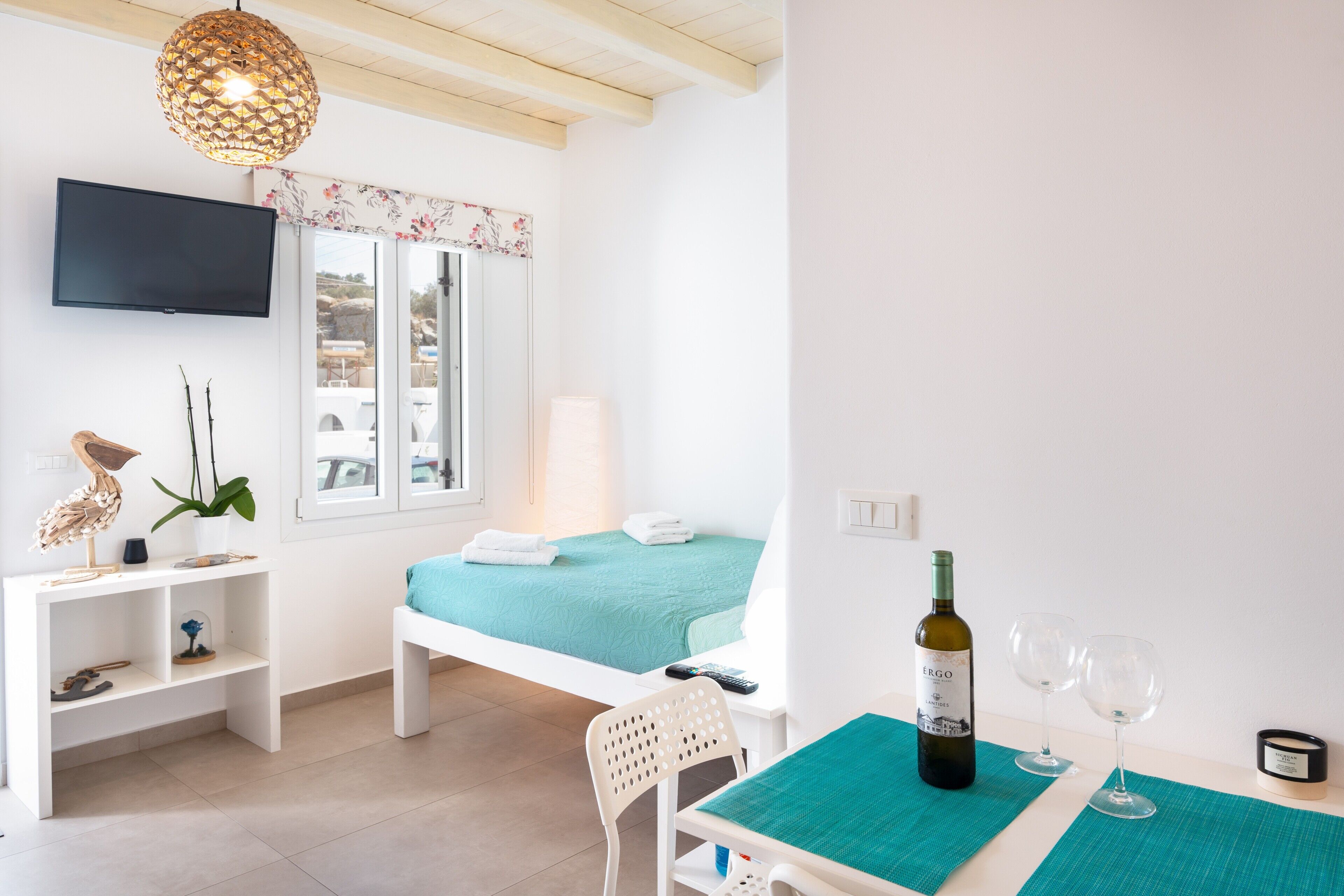 Een slaapkamer met een bed, een televisie, een tafel met een fles en glazen, een stoel en een plank met decoratieve objecten.