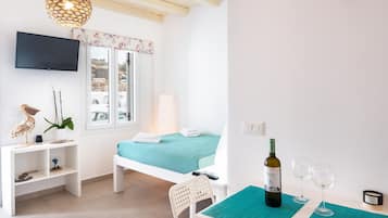 Een slaapkamer met een bed, een televisie, een tafel met een fles en glazen, een stoel en een plank met decoratieve objecten.