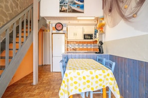 A compact kitchen with a dining table, a clock, and a view of boats through a window.