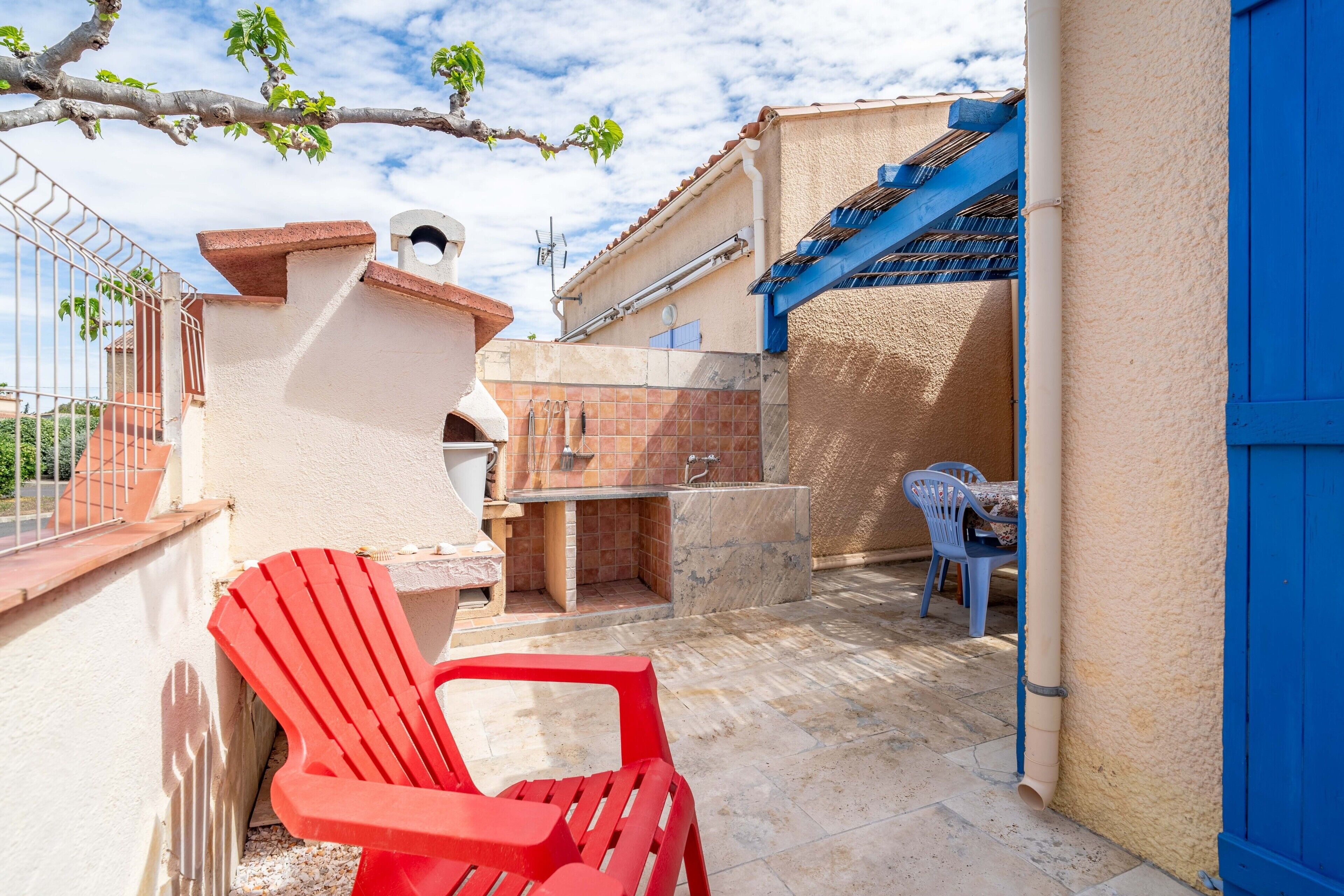 A patio with a barbecue, red chairs, and a blue door.