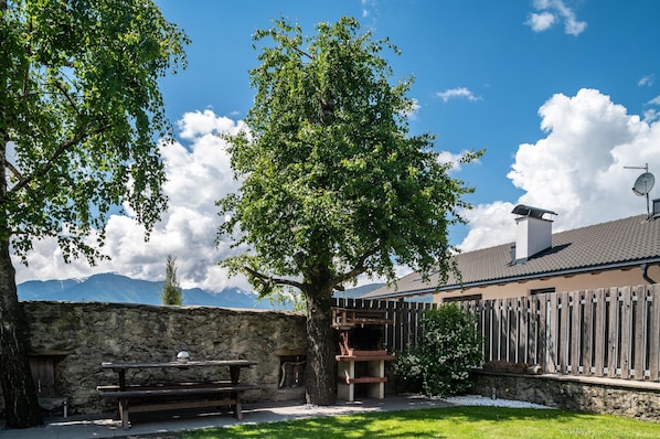 A stone wall, wooden fence, picnic table, and a tree in a backyard with a mountain view.