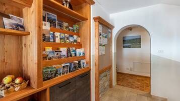 A wooden bookshelf with travel brochures, a small display of apples and nuts, and a view through an archway to a landscape.