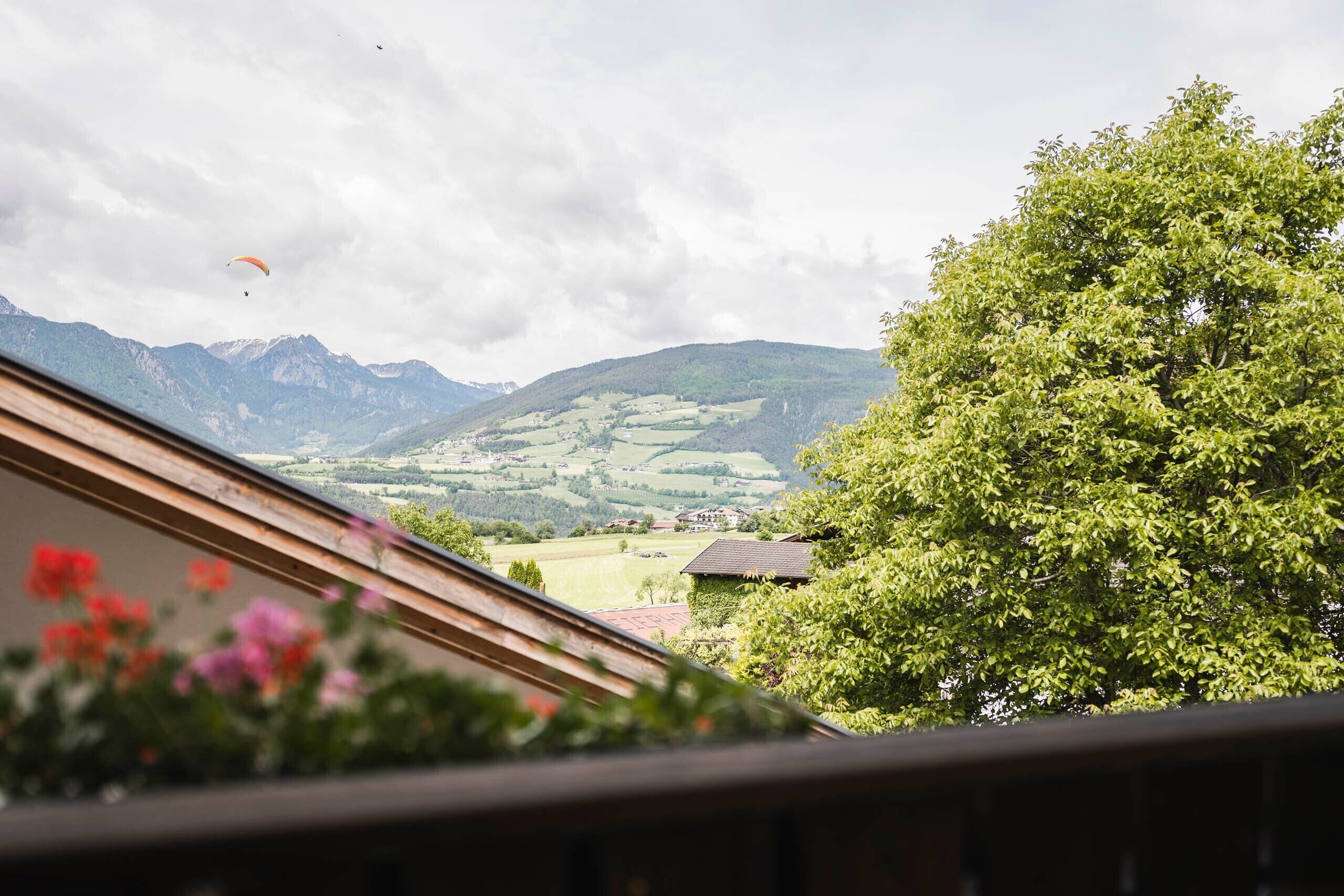A view of a mountainous landscape with a house and a tree in the foreground.