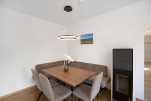 Un coin repas avec une table en bois, quatre chaises grises, un vase de fleurs, un luminaire suspendu moderne, un tableau au mur et un four encastré.