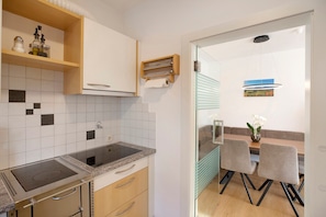 Une cuisine moderne dotée d’une cuisinière intégrée, d’une étagère en bois où sont rangés des ustensiles de cuisine, et d’un coin repas avec une table et des chaises.