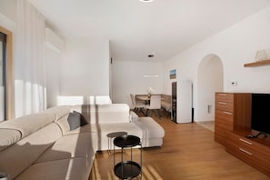 A modern living room with a sofa, a dining area, and a TV stand.