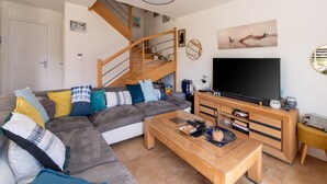 Una sala de estar moderna con un sofá seccional gris, una mesa de centro de madera, un mueble para televisor y una escalera.