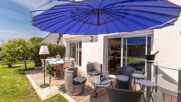 Un patio al aire libre con mobiliario de mimbre, una mesa con superficie de vidrio y un gran paraguas azul.