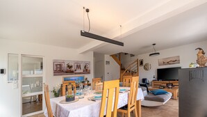 Comedor con una mesa dispuesta para cuatro, sillas de madera, mantel blanco y una lámpara colgante moderna.