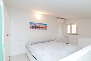 Un dormitorio con cama, cómoda, aire acondicionado instalado en la pared, ventana y un cuadro.