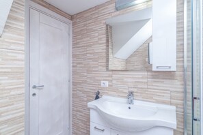 Un baño con un lavamanos blanco, un espejo y una puerta.