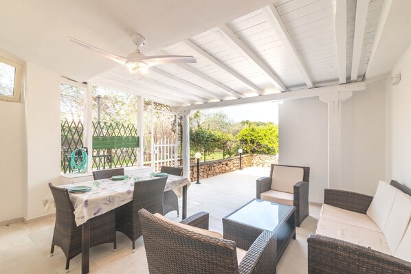 Un patio exterior con mobiliario de mimbre, una mesa y un ventilador de techo.