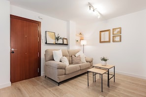 A living room with a sofa, a small table, a lamp, and framed artwork on the wall.