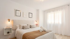 Ein ordentlich bezogenes Bett mit einer braunen Decke, weißen Kissen und einem weißen Kopfteil. An beiden Seiten des Bettes befinden sich Wandleuchten.