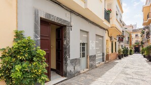 Eine enge Straße mit Gebäuden an beiden Seiten, ein Blumentopf im Vordergrund und ein geschlossener Laden mit einer Marmoreingangstür.