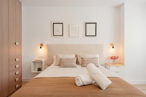 A neatly arranged bedroom with a bed, bedside tables, a wardrobe, and wall-mounted artwork.
