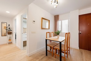 A dining area with a wooden table and chairs, a mirror on the wall, and a door to the right.