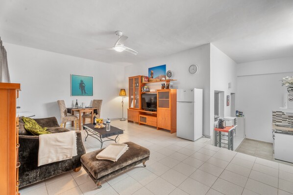 A living room with a sofa, ottoman, TV stand, and dining area.
