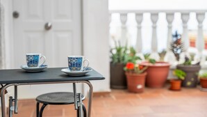 Una mesa con dos tazas y platillos, una silla y plantas en macetas en un balcón.
