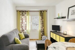 Una sala de estar con un sofá, una mesa, un televisor y un mueble aparador.