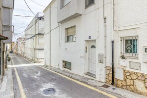 Eine schmale Straße mit weißen Gebäuden, einer sichtbaren Tür mit Hausnummer und einer Steinmauer.