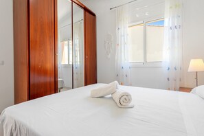 Una habitación de hotel con cama, armario de madera, ventana con cortinas y lámpara de noche.