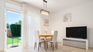 A modern living room with a dining table, chairs, a flat-screen TV, and a sliding glass door to a garden. - Holiday Home 'Isla Bonita' with Sea Views, Wi-Fi and Air Conditioning (Mont-roig del Camp)