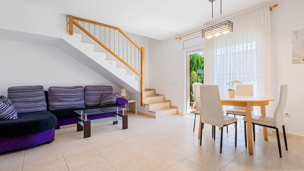 A living room with a sofa, a dining table with chairs, a staircase, and a view of greenery outside. - Holiday Home 'Isla Bonita' with Sea Views, Wi-Fi and Air Conditioning (Mont-roig del Camp)